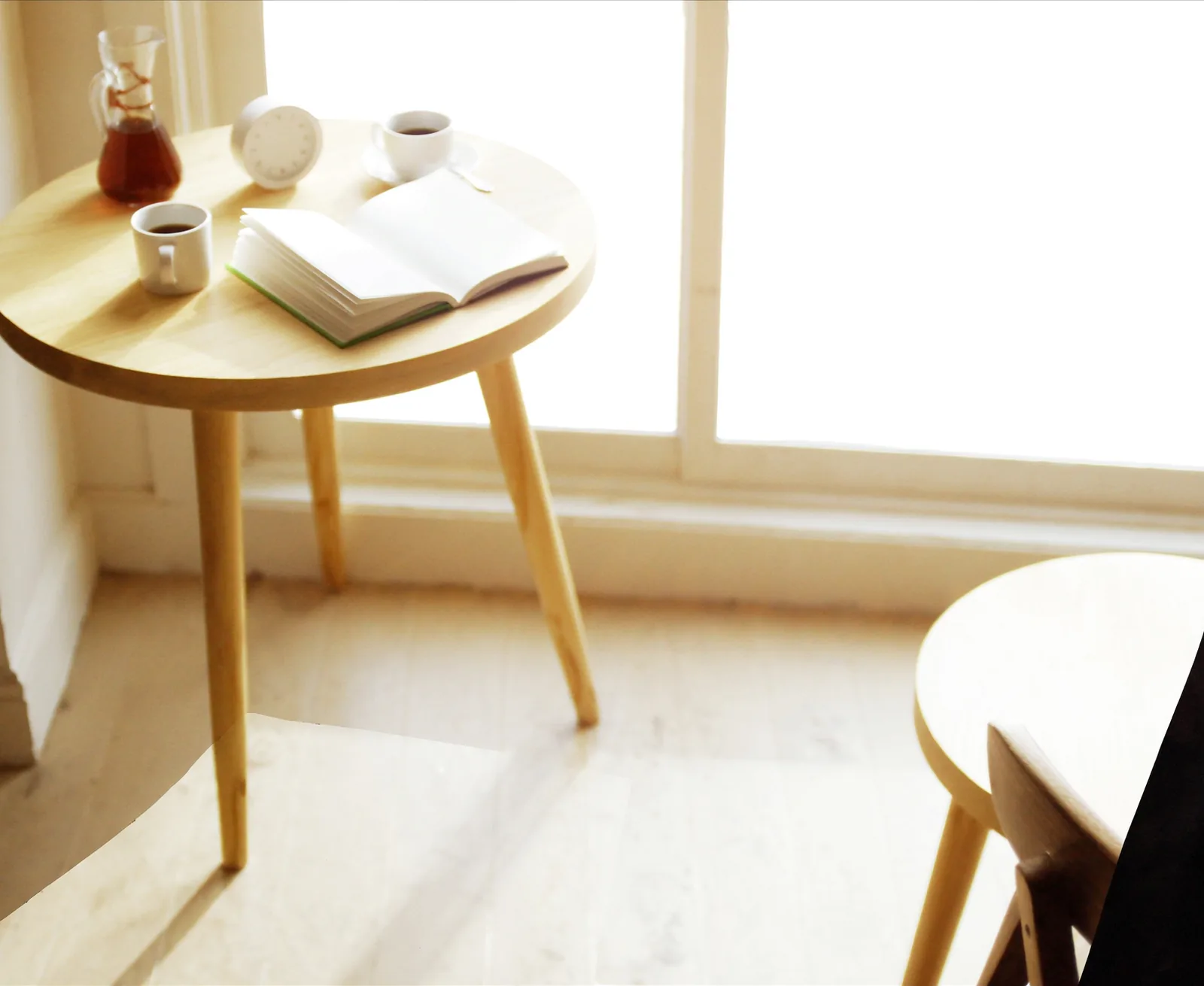 Une petite table ronde près d’une fenêtre, deux tasses de café et un carnet ouvert.